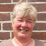 Die stolze Weiterbildungsteilnehmerin Astrid Estel steht, die Hände auf die Hüften gestützt, vor einer geziegelten Hauswand.